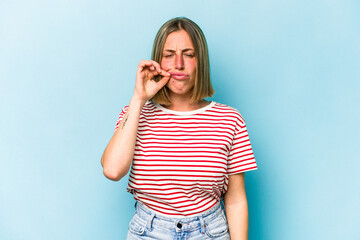 Young caucasian woman isolated on blue background with fingers on lips keeping a secret.