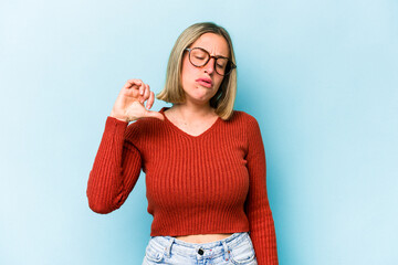 Young caucasian woman isolated on blue background showing a dislike gesture, thumbs down....