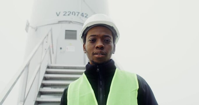 A man smiles looking at the camera, standing near an industrial wind turbine