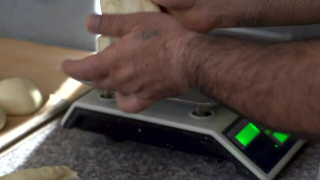 Baker cutting and measuring dough on weighing scale. Process of making bread at bakery