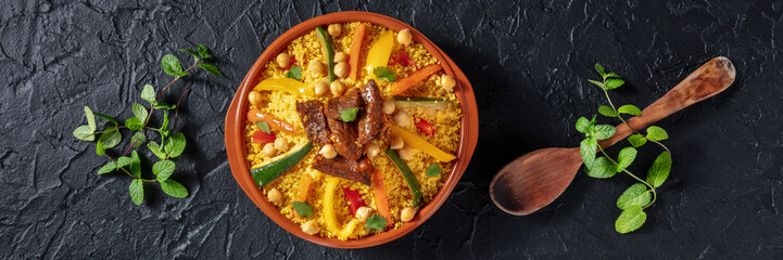 Meat and vegetable couscous panorama. Traditional Moroccan dish, overhead flat lay shot on a dark background