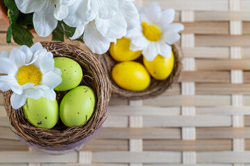 Easter green, yellow eggs with spots and chamomile flowers in a small basket on a wicker surface. Greeting cards for Easter. Shallow depth of field. Top view.