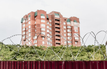 Barbed wire on fence with modern residential building on background. Protection and prohibition concept.