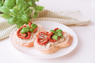 Traditional italian appetizer - bruschetta or toast with ricotta cheese and sliced sun dried tomatoes topped with basil on white table background. Delicious italian appetizer