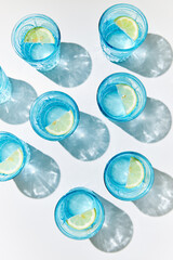 Detox lemon water in blue glasses with fresh lemons, sunlight and shadows.