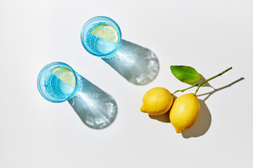 Detox lemon water in blue glasses with fresh lemons, sunlight and shadows.