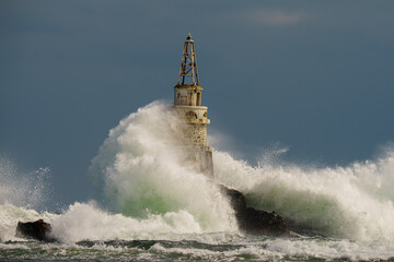 Old rusty lighthouse in the Black Sea with giant waves crashing on it in Ahtopol, Bulgaria