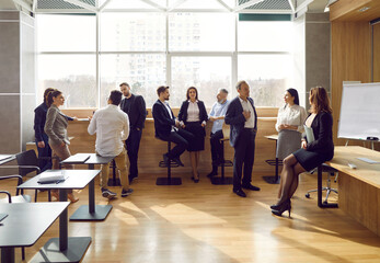 Different men and women standing in modern office and talking. Diverse people gather in groups and...
