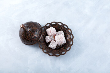 Lokum or Turkish delight, oriental sweets in brown metal serving bowl on grey textured background, top view. Selective focus
