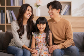 Obraz premium Happy parents and little daughter having fun enjoying spending leisure time together at home sitting on sofa.