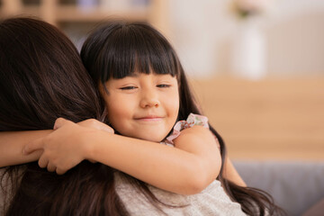 Asian Mum her little daughter hugging sit on sofa smile.Loving family portrait, Mothers Day celebration concept .