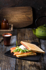 Toast with salmon, poached egg and guacamole. Breakfast on a wooden table, served with a kettle, shot, spices and herbs.Сlose up. Restaurant, cafe, bar menu.