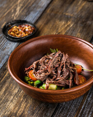 Deep plate with hot vegetables and beef. On a wooden table is a mug of light beer, spices and tomatoes. Menu for bar, cafe, restaurant. Dish from the chef. Close up