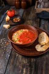 Brown plate of tomato soup with parmesan, microgreens and toast. On a wooden background spices, cheese, tomato. For the menu of the restaurant, cafe, bar. Close up.