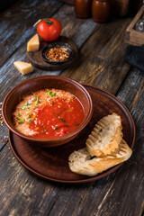 Brown plate of tomato soup with parmesan, microgreens and toast. On a wooden background spices, cheese, tomato. For the menu of the restaurant, cafe, bar. Close up.