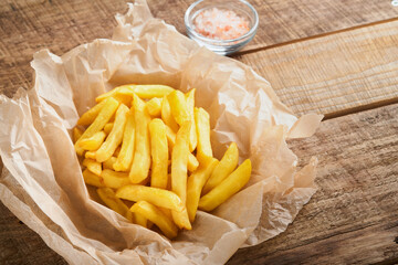 French fries. Tasty French fries server on parchment paper on wooden cutting board with tomato and cheese sauce on wooden table background. Diverse Keto Dishes. Fast food and unhealthy food concept.