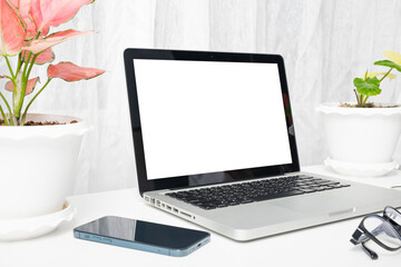 Fototapeta premium Modern workspace, mock up laptop computer blank white screen, eyeglasses and smartphone white table have potted plants on the desk, Notebook and mobile phone on desktop home office