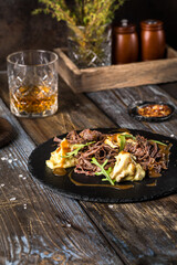 On a round serving board, mashed potatoes with beef in mushroom sauce, with herbs. On a wooden table is spices, mushrooms, a glass of cognac. Close up. For the menu of a restaurant, cafe, bar