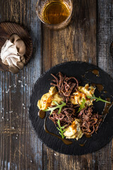 On a round serving board, mashed potatoes with beef in mushroom sauce, with herbs. On a wooden table is spices, mushrooms, a glass of cognac. Top view. For the menu of a restaurant, cafe, bar