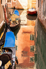 Fototapeta na wymiar canal in small alley of Venice with gondola and colorful water reflections