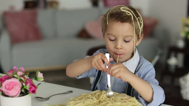 Cute preschool child, blond boy, eating spaghetti at home, making a mess everywhere, funny moments