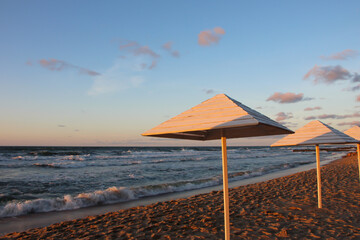 view of beach with umbrellas in stormy weather at sunset in sunny reflexes