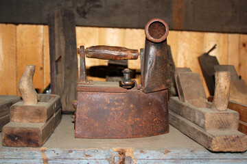 A set of household utensils and tools, including an old rusty charcoal iron with a pipe and wooden planers.