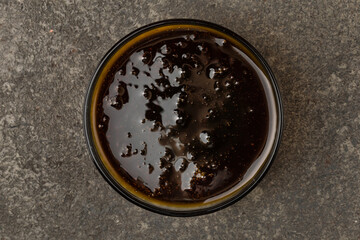 A cup with barbecue sauce on a gray textured background. Top view.