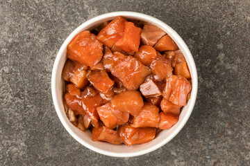 A bowl of sliced salmon in soy sauce on a gray textured background. Top view.