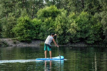 Fototapeta na wymiar A man sup surfing paddling on a boat on the river in summer.