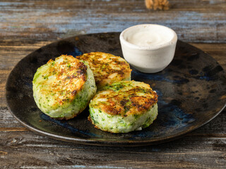 On a blue ceramic plate 3 hash browns with sour cream sauce. Brown wooden background. Close up