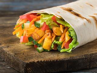 Vegetarian shawarma in lavash with cucumbers, potatoes, carrots, tomatoes, lettuce leaves. On a wooden brown background. Close up.