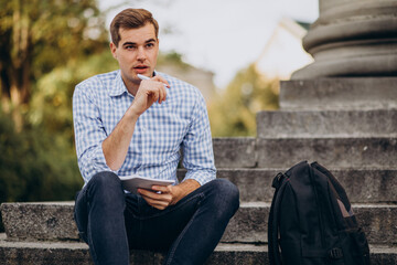 Obraz premium Handsome student sitting on stairs of university and studying