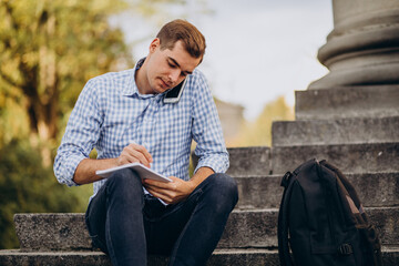 Obraz premium Handsome student sitting on stairs of university and studying