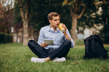 Young male student studying in park and sitting in park