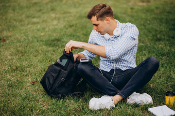 Naklejka na ściany i meble Young male student studying in park and sitting in park