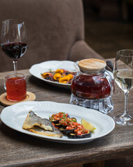On the table in the restaurant serving for 2 persons. Dish with fish and eggplant, a glass teapot with red tea, a mug of tea, a glass of white and red wine, a plate with carpaccio in the background.