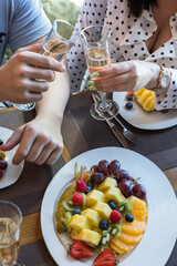 A girl and a gay at a table in a restaurant clink glasses of champagne. The table is served with fruit and berries.