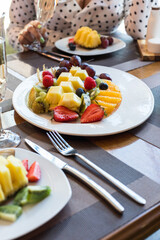 A girl and a gay at a table in a restaurant clink glasses of champagne. The table is served with fruit and berries.