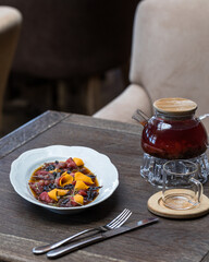 Oval plate with beef carpaccio with prunes, wine, sweet potatoes and micro greenery. On a wooden...