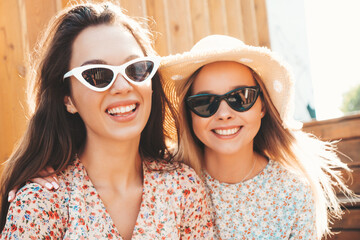 Two young beautiful smiling hipster female in trendy summer dresses.Sexy carefree women posing in the street. Positive pure models having fun at sunset, hugging and going crazy