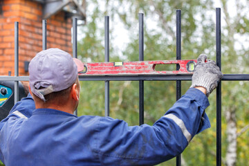 Naklejka premium The builder uses an old level to level the metal fence when it is being installed.
