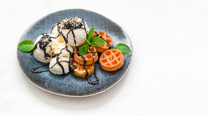 ice cream with waffles, chocolate syrup and fresh mint on a dark platter. copy space