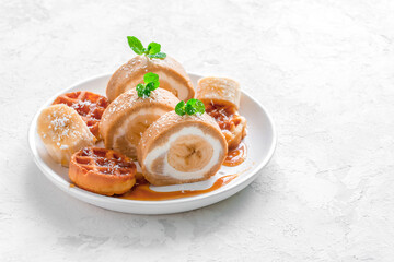 banana roll with waffles and caramel syrup on a white dish