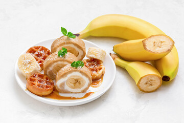 banana roll with waffles and caramel syrup on a white dish