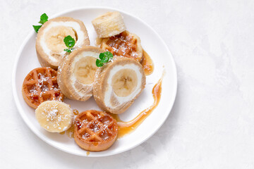 banana roll with waffles and caramel syrup on a white dish. view from above