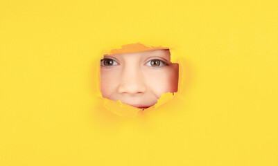 Breaking paper background. Emotions concept. Kid with toothy smile shows face in paper hole. Positive child with toothy pleasant smile on face, keeps through torn hole in yellow paper