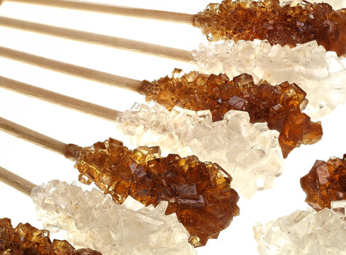 Brown and white candied sugar on wooden sticks, on white background