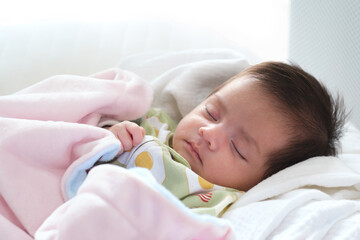 Close up portrait of cute adorable baby girl on white bed in bedroom. Newborn child relaxing sleeping and smiling in the bed in children nursery. Family morning at home.