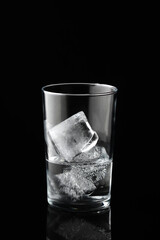 Cold water and ice cubes in glass on black background